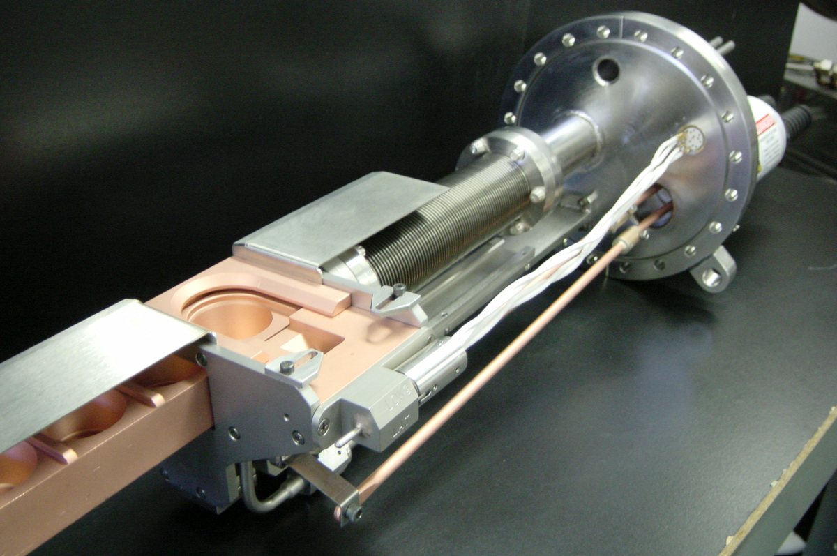 EB6 linear ultra-high-vacuum source: water-cooled copper trough with four pockets and shield plates, on a sliding shaft with bellows, mounting flange, and high-voltage feedthrough.